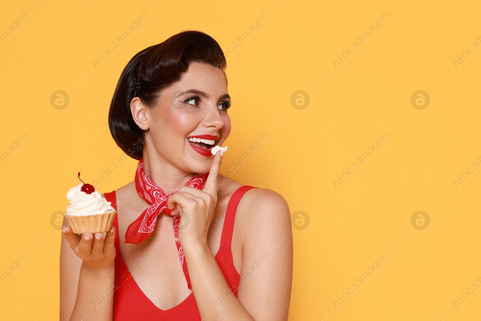 Photo of Pin-up woman eating cupcake on orange background, space for text