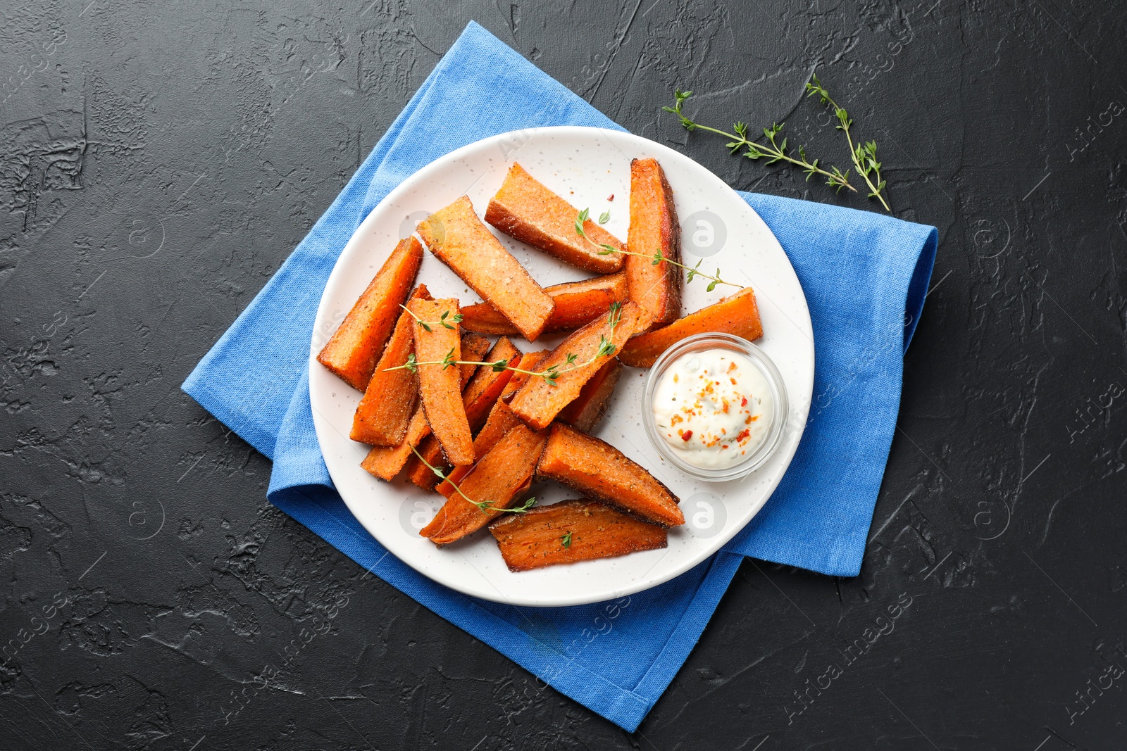 Photo of Pieces of tasty baked sweet potato with microgreens and sauce on grey textured table, flat lay