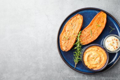 Photo of Halves of tasty baked sweet potato served with sauces on grey textured table, top view. Space for text