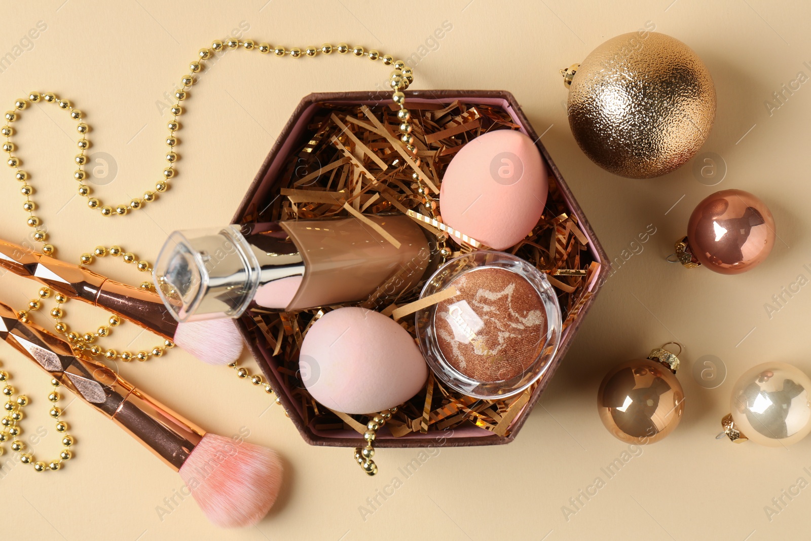 Photo of Christmas gift box with cosmetic products and festive decor on beige background, flat lay