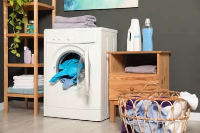 Photo of Washing machine, detergents and basket with laundry in room