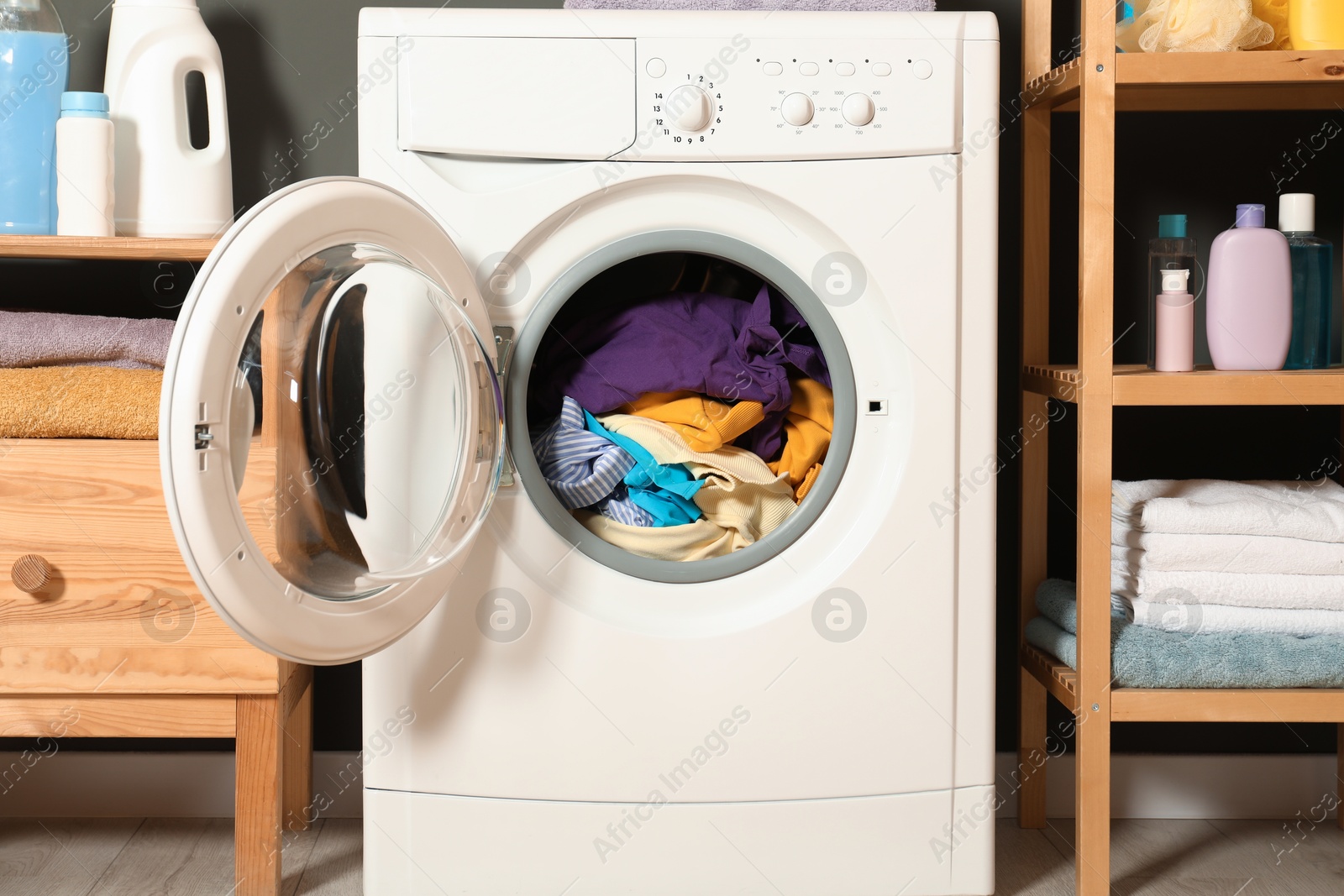 Photo of Washing machine, detergents and towels indoors, closeup