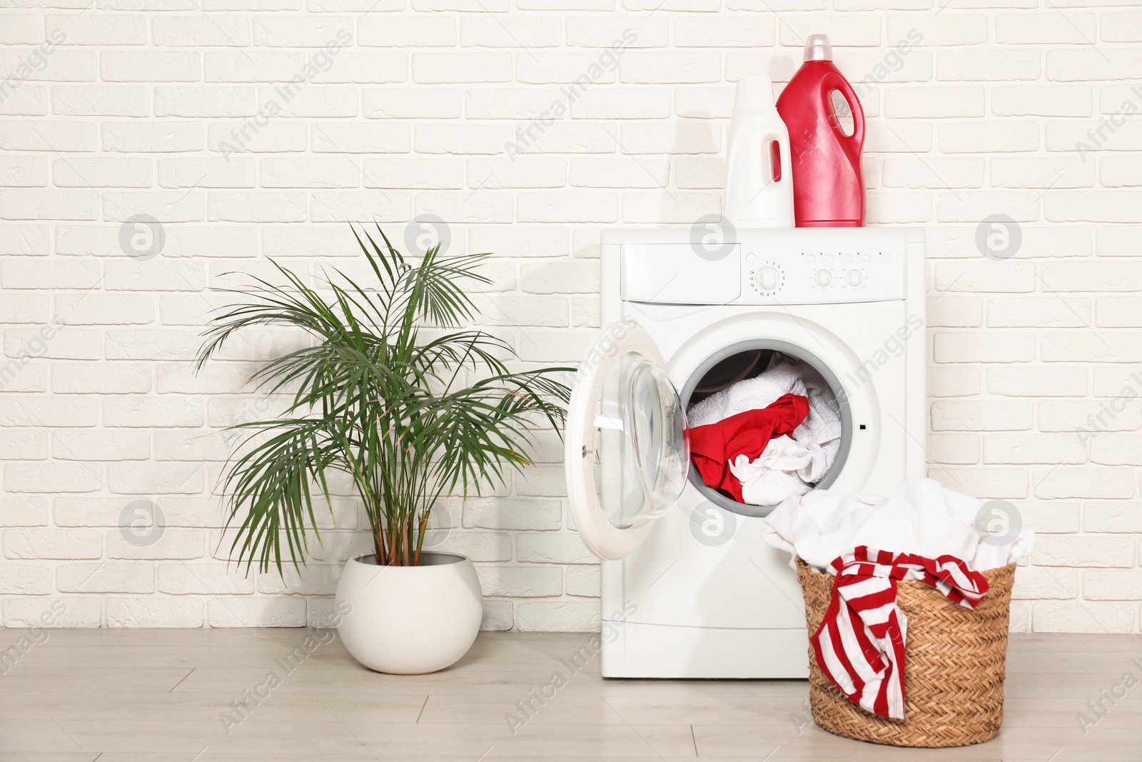 Photo of Washing machine, detergents and basket with laundry in room