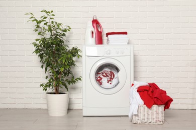 Photo of Washing machine, detergents and basket with laundry in room