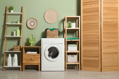 Photo of Washing machine, detergents and basket with laundry in room