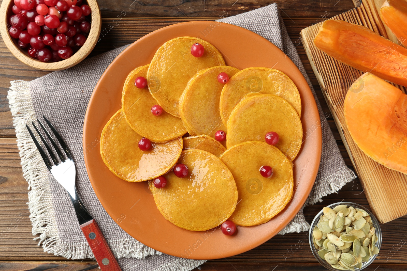 Photo of Tasty pumpkin pancakes with cranberries served on wooden table, flat lay