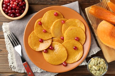 Photo of Tasty pumpkin pancakes with cranberries served on wooden table, flat lay