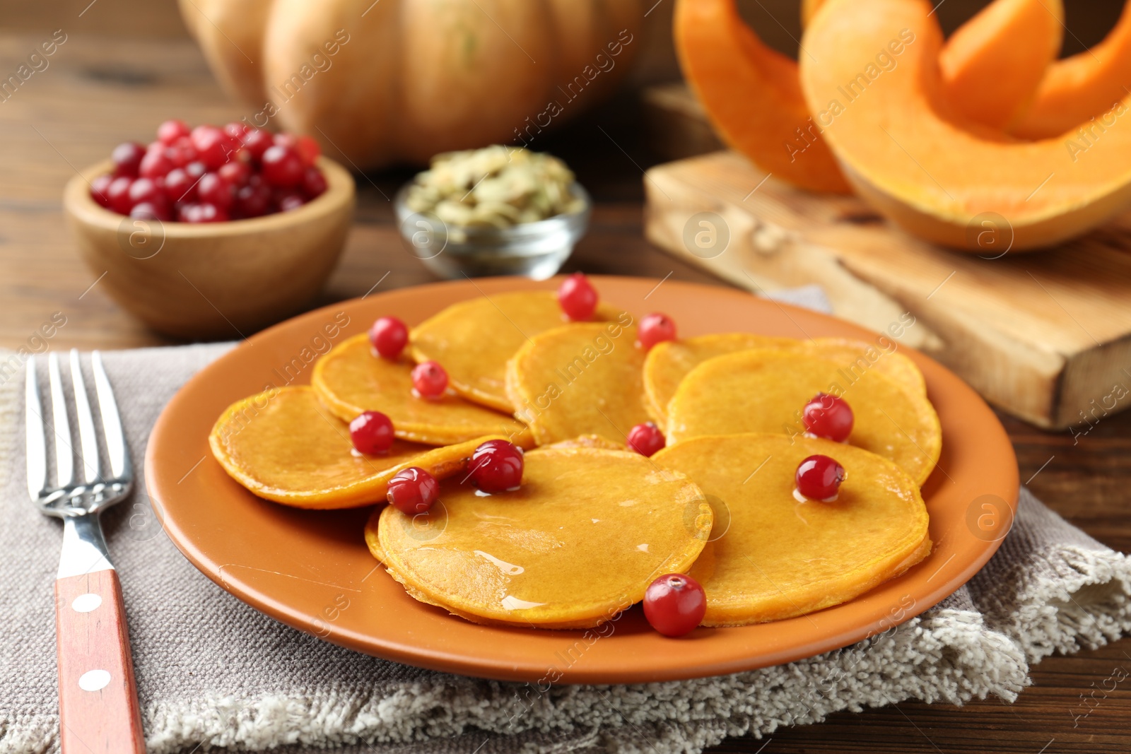 Photo of Tasty pumpkin pancakes with cranberries served on wooden table, closeup