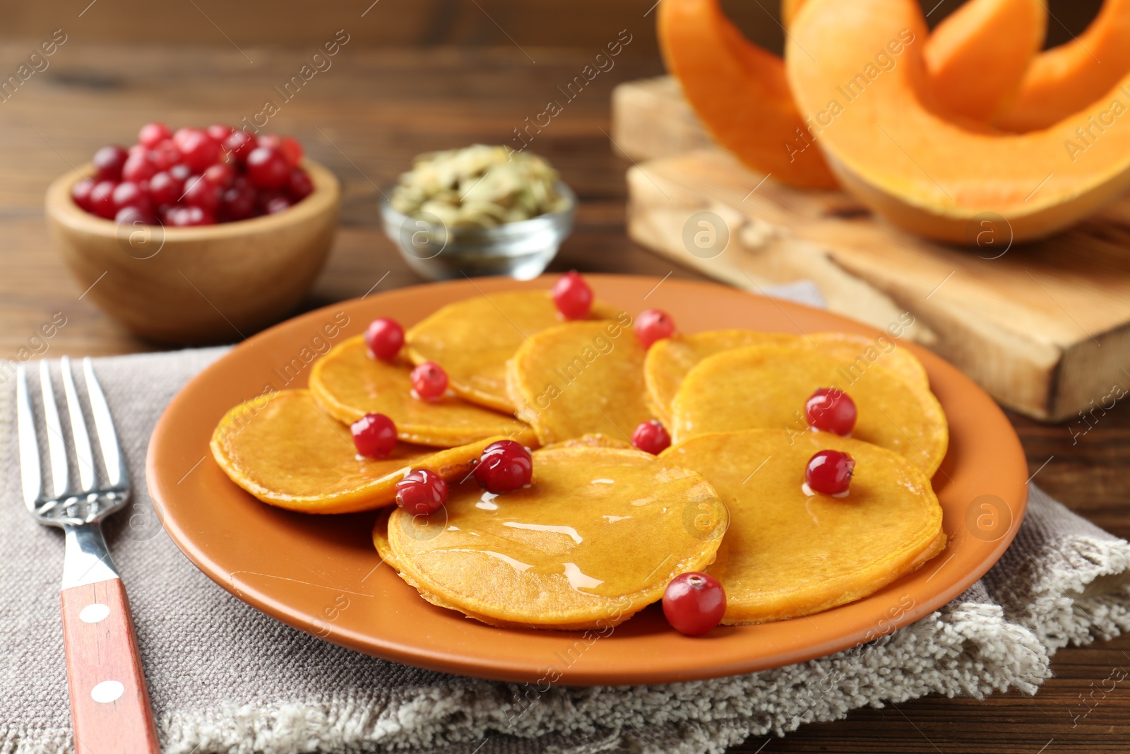 Photo of Tasty pumpkin pancakes with cranberries served on wooden table, closeup