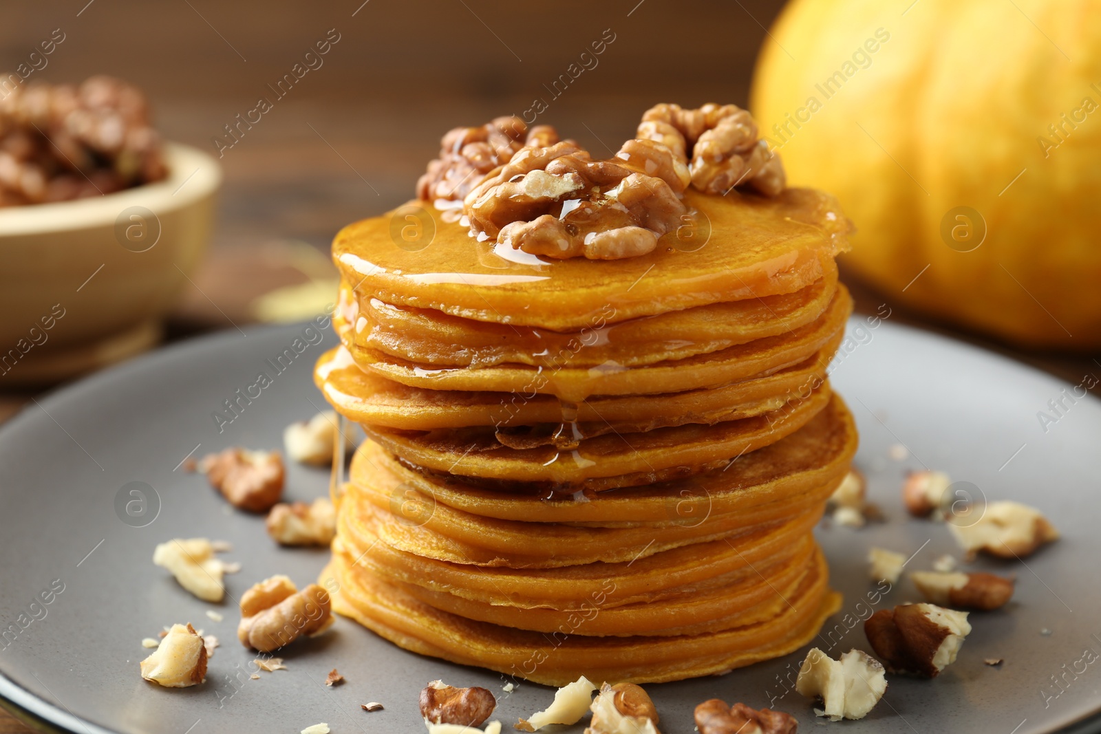 Photo of Tasty pumpkin pancakes with honey and walnuts on table, closeup