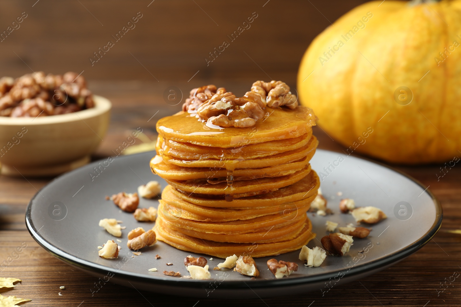 Photo of Tasty pumpkin pancakes with honey and walnuts on wooden table, closeup