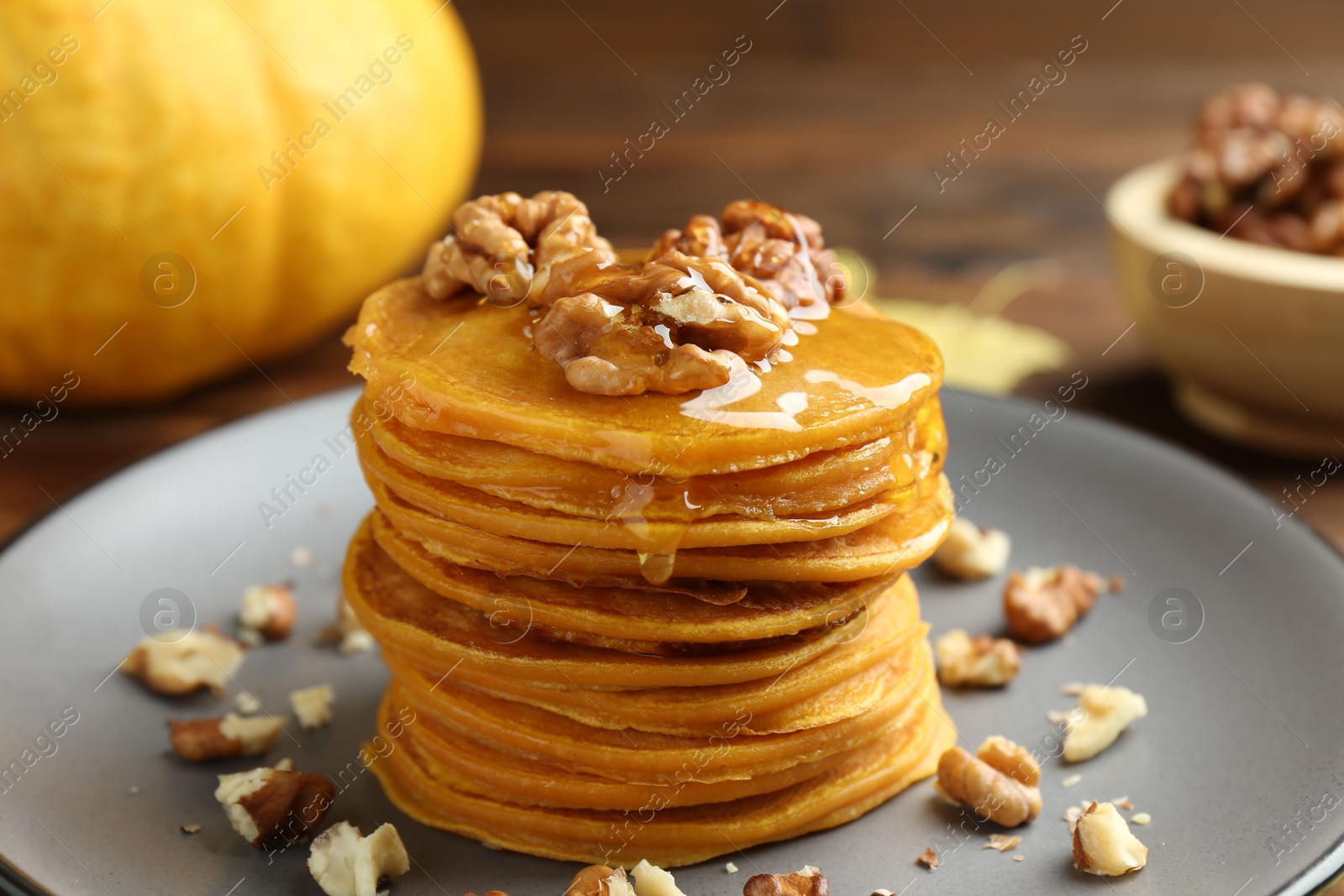 Photo of Tasty pumpkin pancakes with honey and walnuts on table, closeup