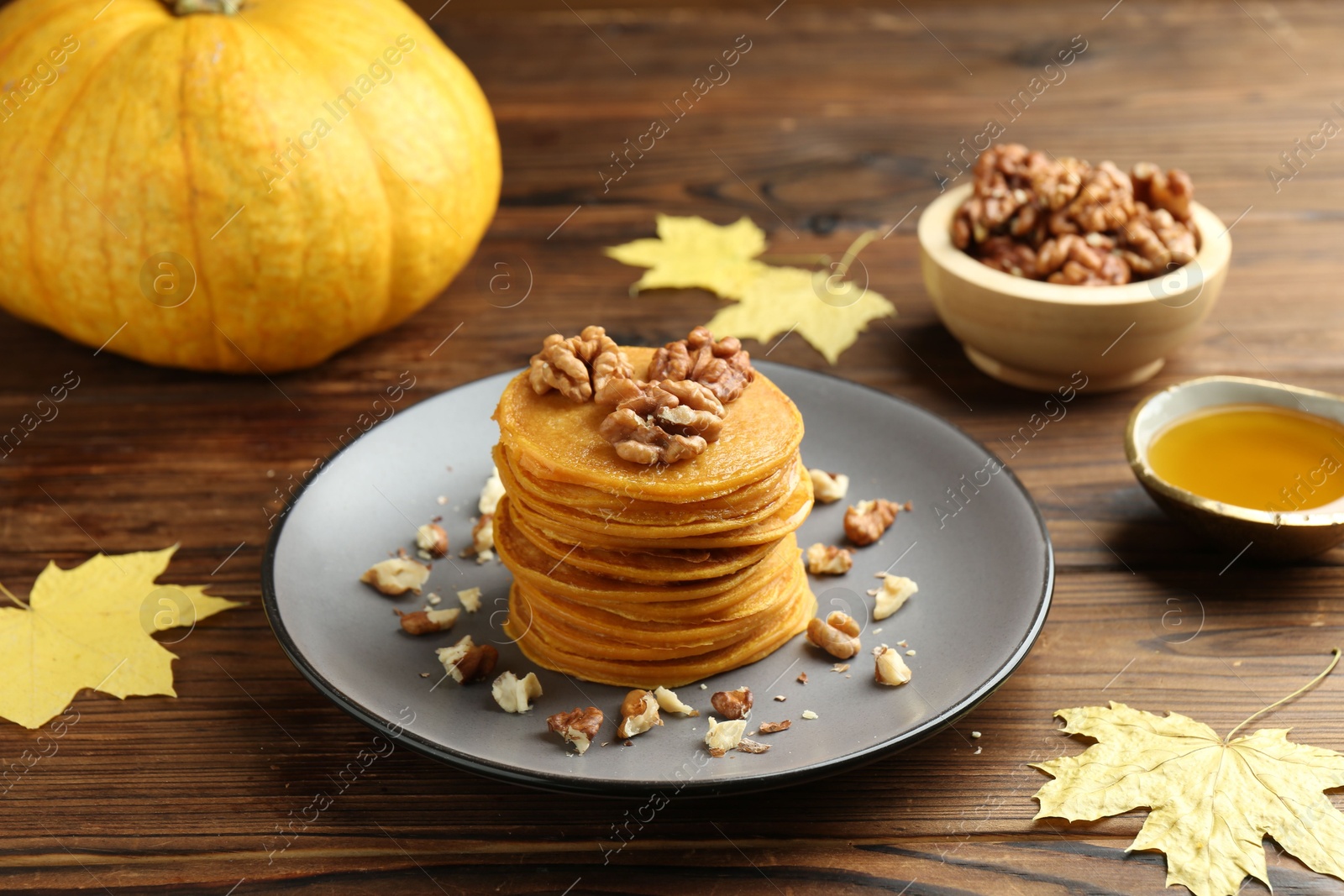 Photo of Tasty pumpkin pancakes with nuts, honey and maple leaves on wooden table