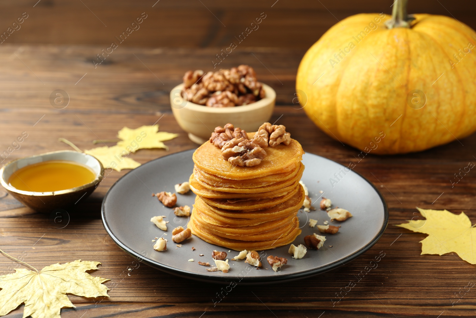 Photo of Tasty pumpkin pancakes with nuts, honey and maple leaves on wooden table