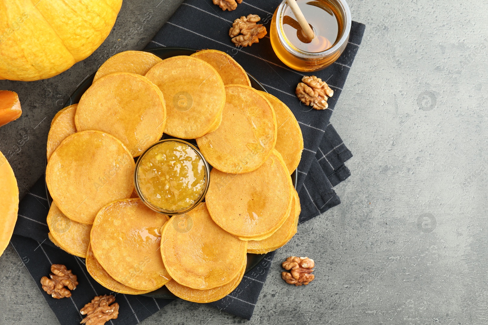 Photo of Tasty pumpkin pancakes with honey, walnuts and jam on grey table, flat lay. Space for text