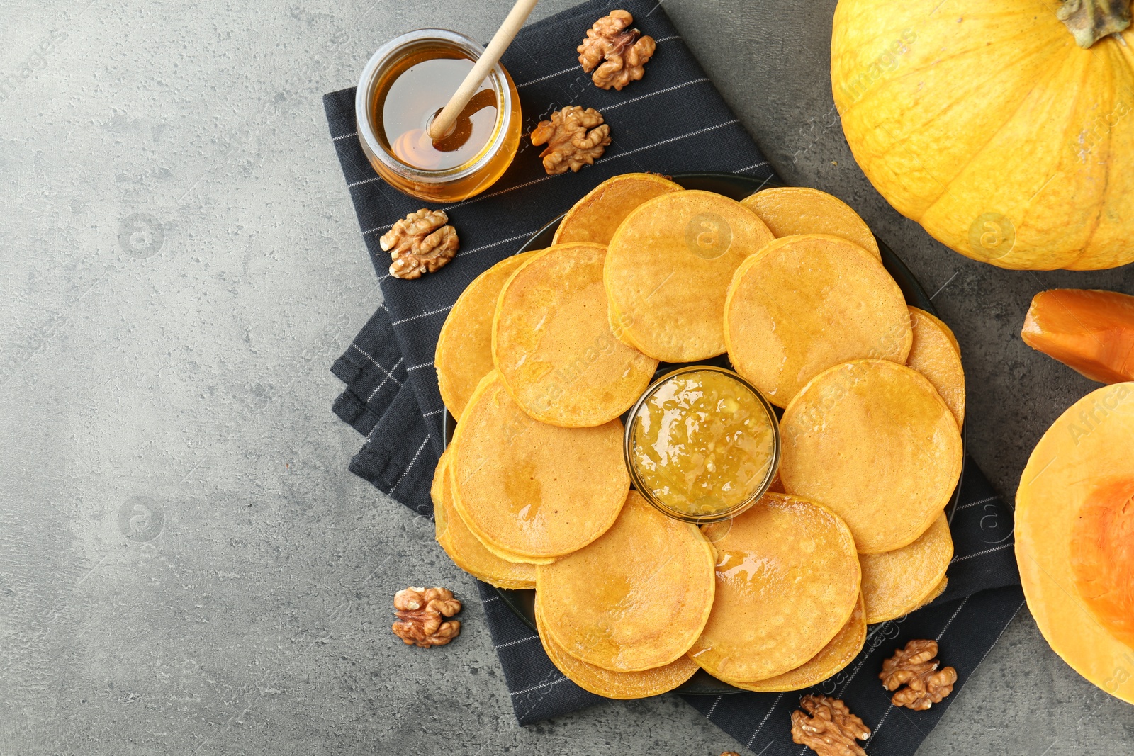 Photo of Tasty pumpkin pancakes with honey, walnuts and jam on grey table, flat lay. Space for text