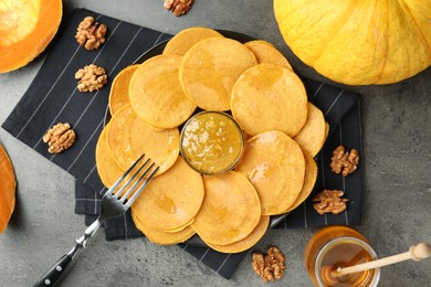 Photo of Tasty pumpkin pancakes with honey, walnuts and jam on grey table, flat lay