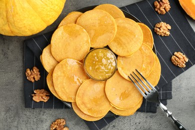 Photo of Tasty pumpkin pancakes with walnuts and jam on grey table, flat lay