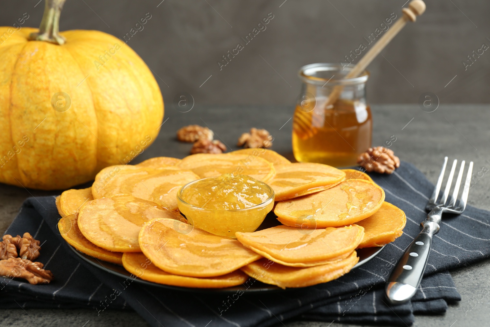 Photo of Tasty pumpkin pancakes with honey, walnuts and jam on grey table, closeup