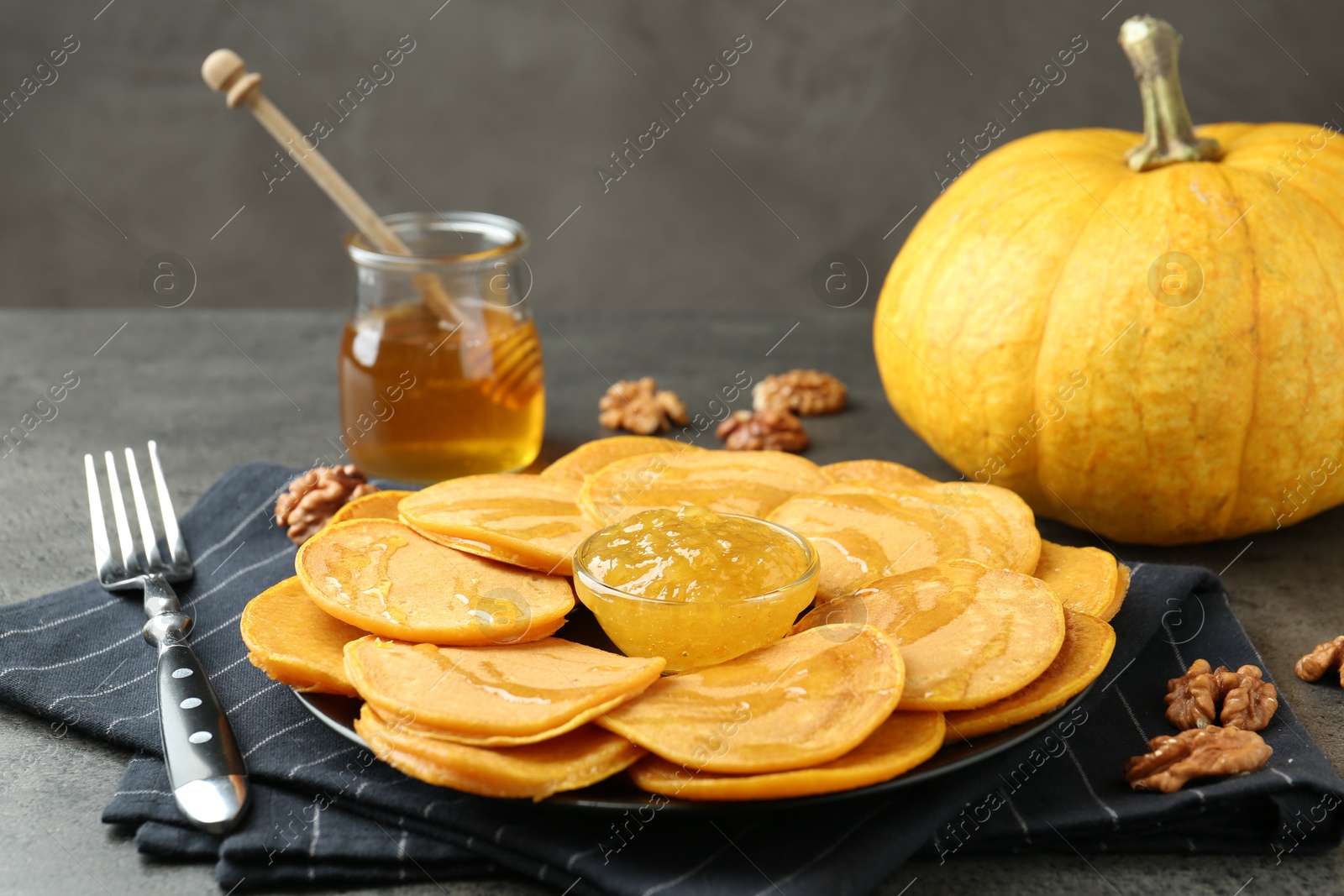 Photo of Tasty pumpkin pancakes with honey, walnuts and jam on grey table, closeup