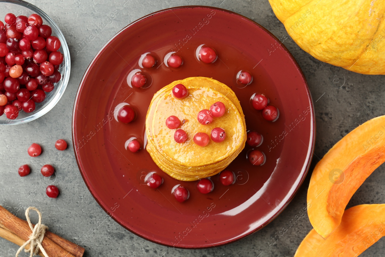 Photo of Tasty pumpkin pancakes with cranberries, honey and cinnamon on grey table, flat lay