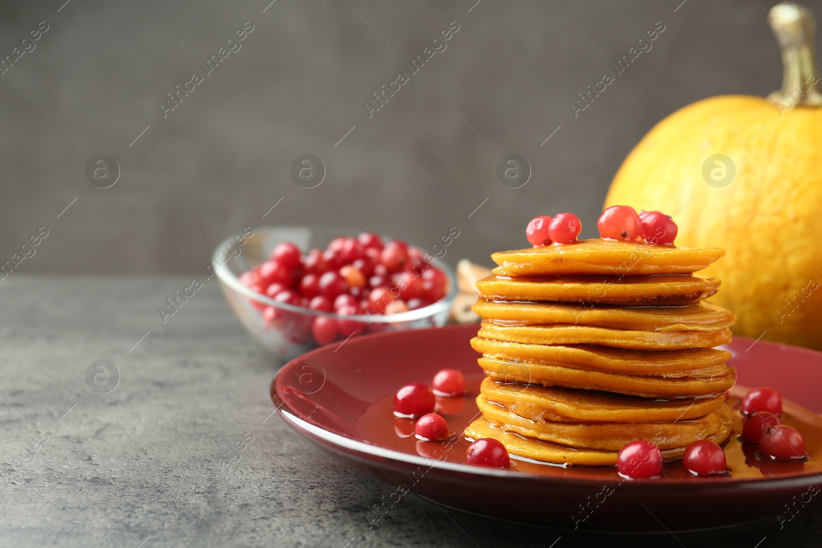 Photo of Tasty pumpkin pancakes with cranberries and honey on grey table, closeup. Space for text