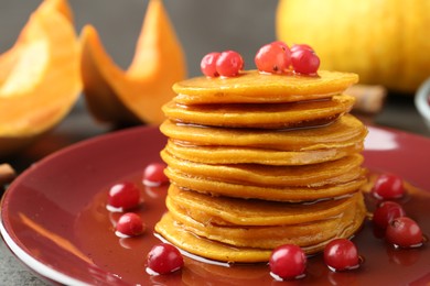 Photo of Tasty pumpkin pancakes with cranberries and honey on table, closeup