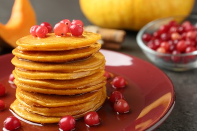 Photo of Tasty pumpkin pancakes with cranberries and honey on table, closeup