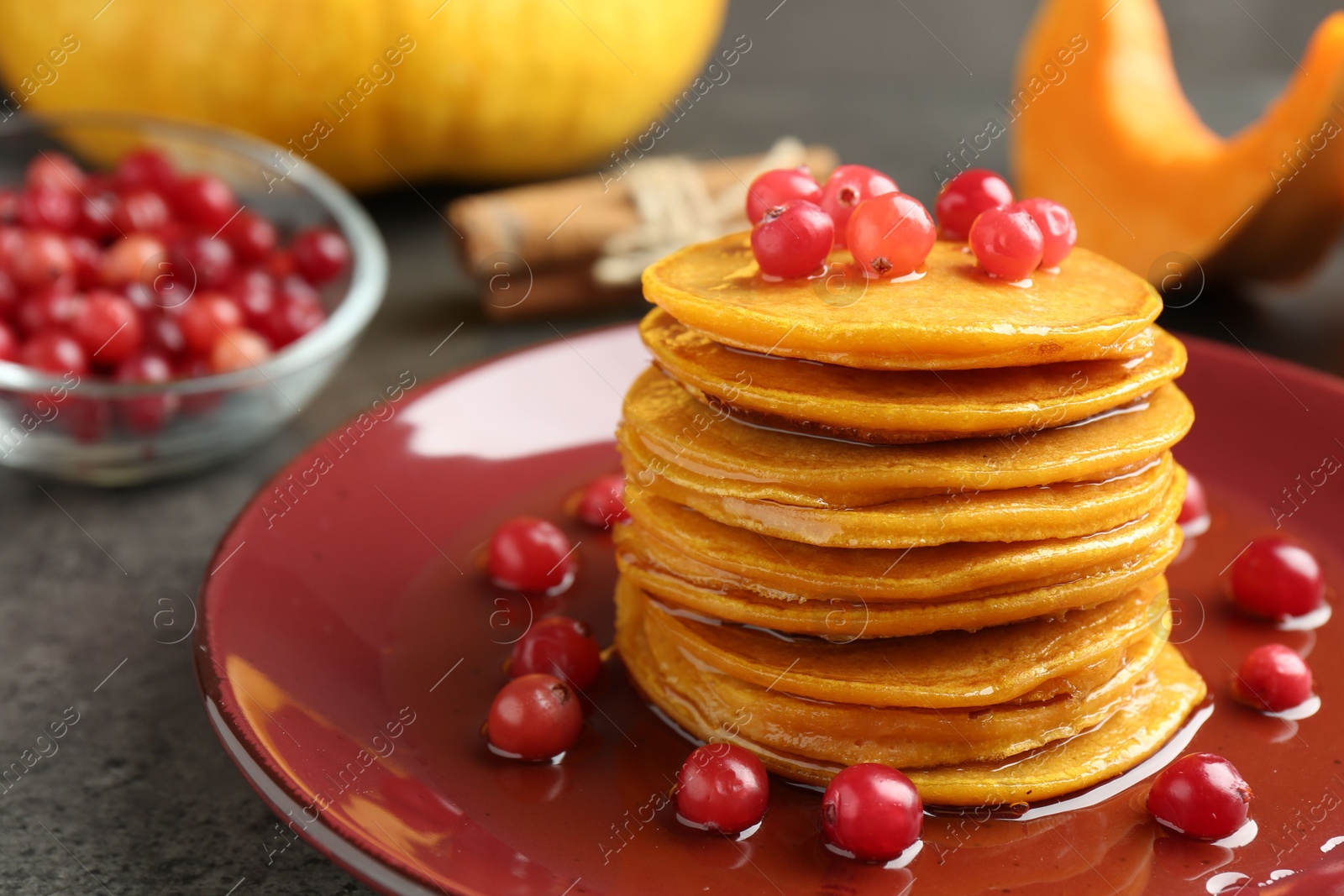 Photo of Tasty pumpkin pancakes with cranberries and honey on grey table, closeup