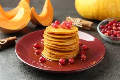 Photo of Tasty pumpkin pancakes with cranberries and honey on grey table, closeup