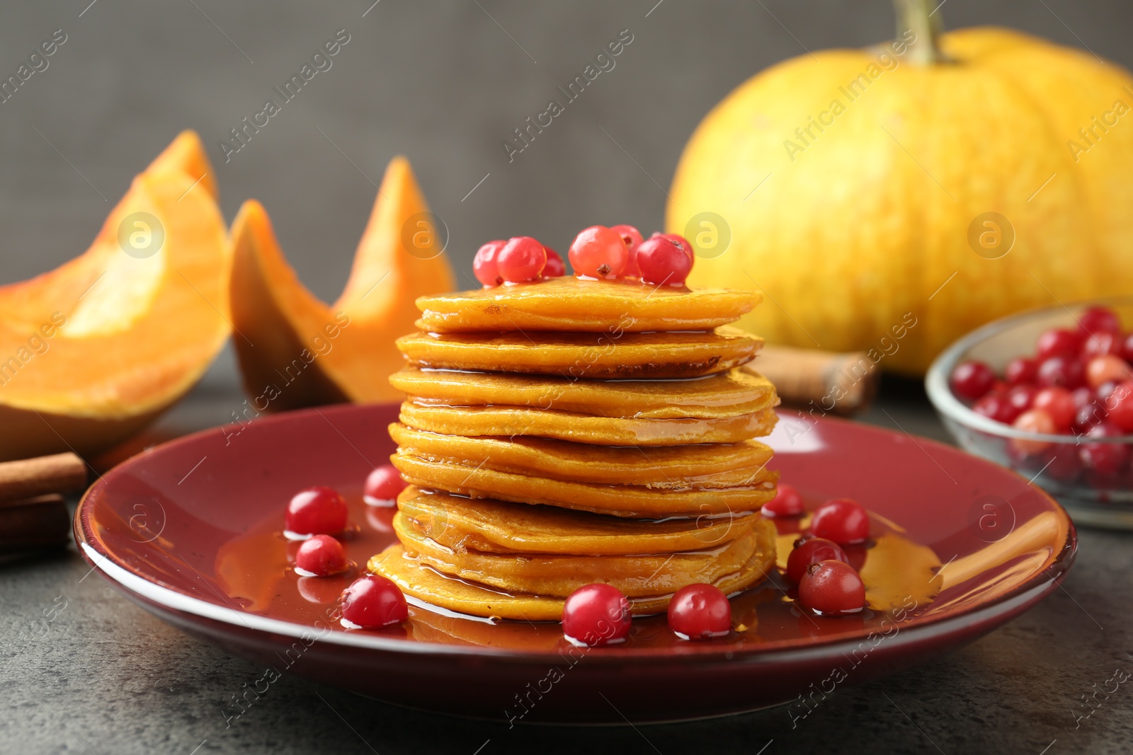 Photo of Tasty pumpkin pancakes with cranberries and honey on grey table, closeup