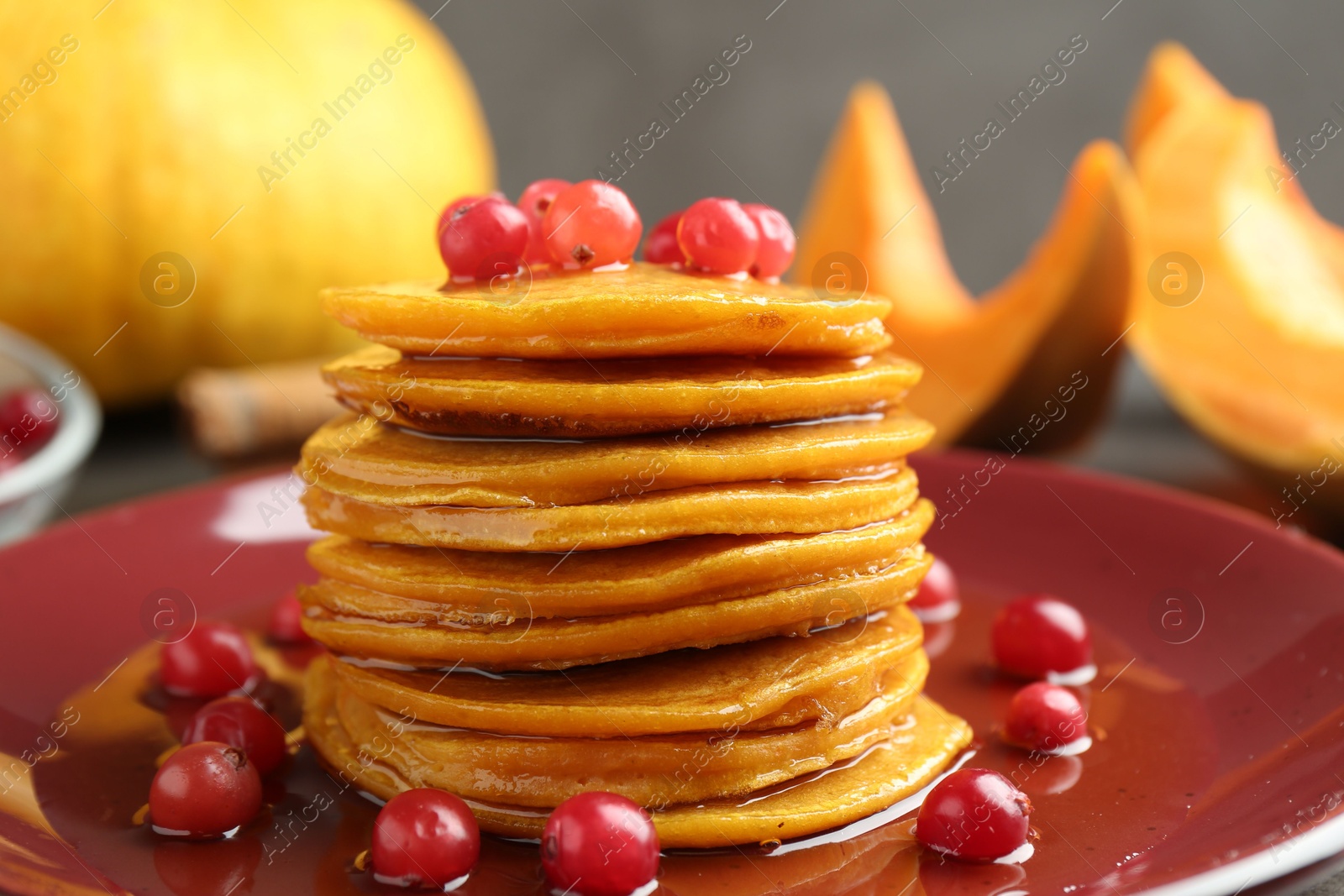 Photo of Tasty pumpkin pancakes with cranberries and honey on plate, closeup