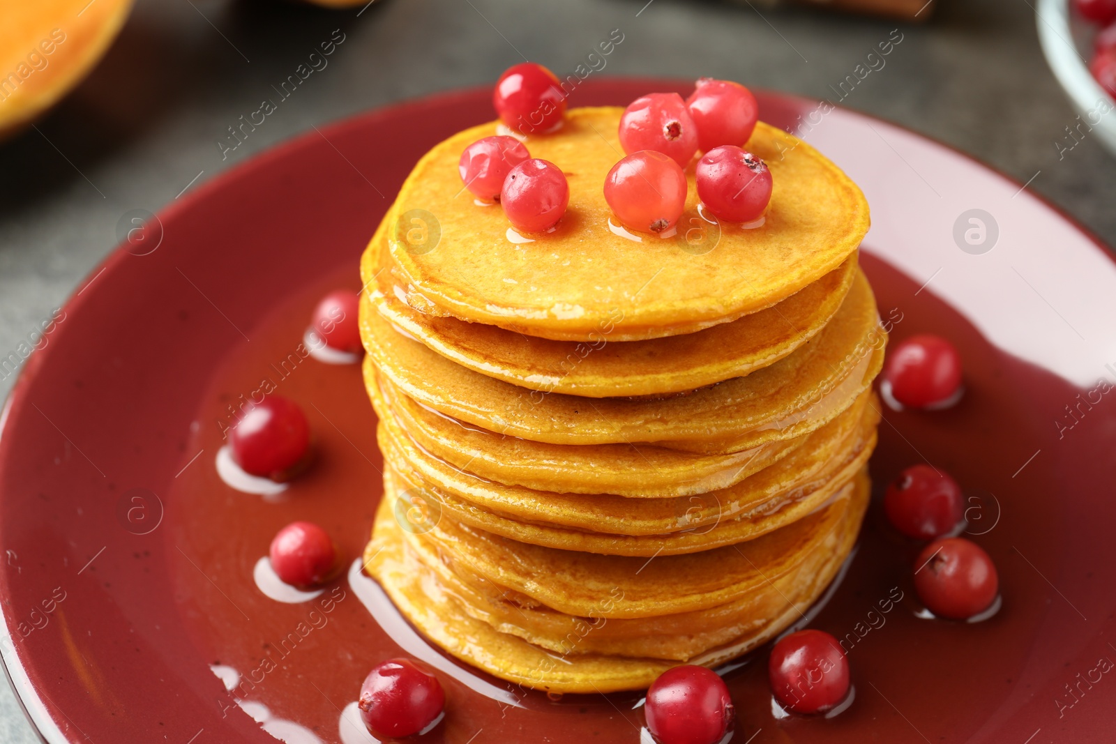 Photo of Tasty pumpkin pancakes with cranberries and honey on table, closeup