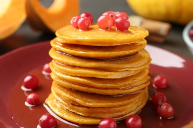 Photo of Tasty pumpkin pancakes with cranberries and honey on plate, closeup