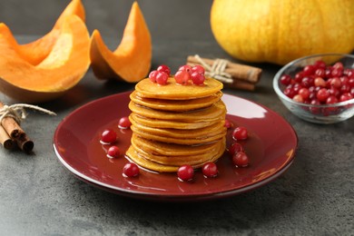 Photo of Tasty pumpkin pancakes with cranberries, honey and cinnamon sticks on grey table, closeup