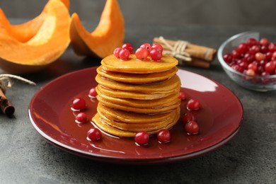 Photo of Tasty pumpkin pancakes with cranberries and honey on grey table, closeup