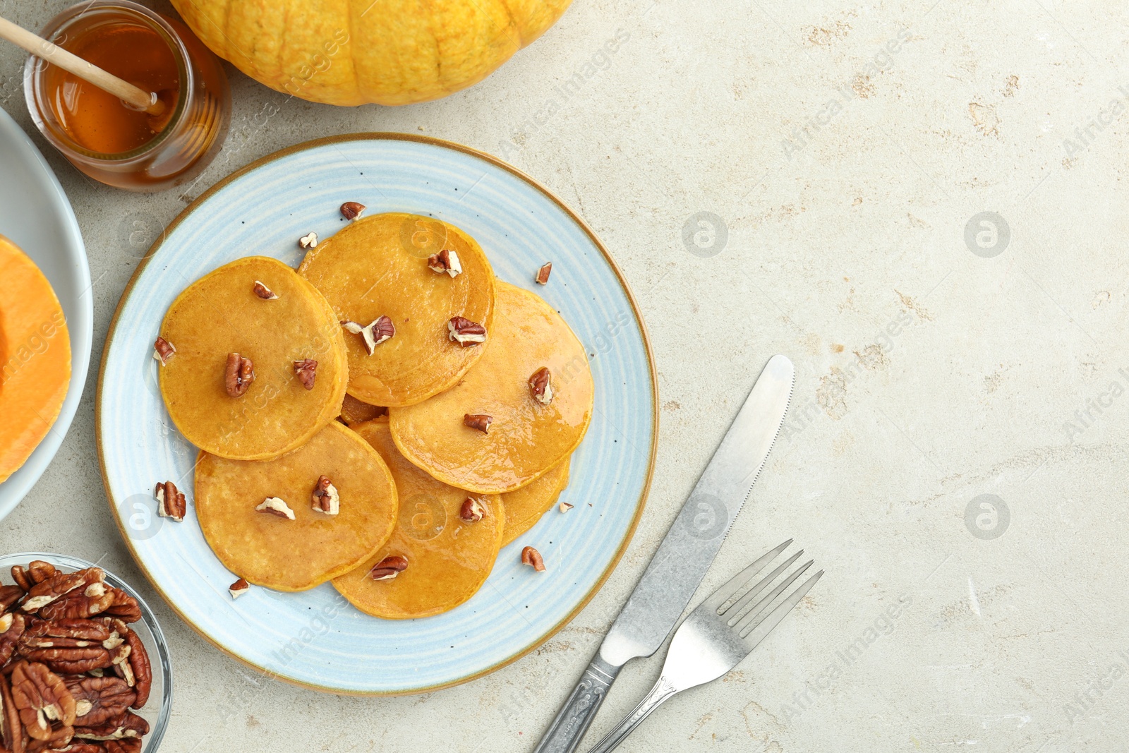 Photo of Tasty pumpkin pancakes with nuts and honey served on light grey table, flat lay. Space for text