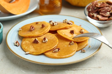 Photo of Tasty pumpkin pancakes with nuts and honey served on light grey table, closeup