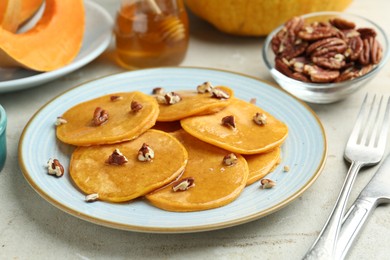 Photo of Tasty pumpkin pancakes with nuts and honey served on light grey table, closeup