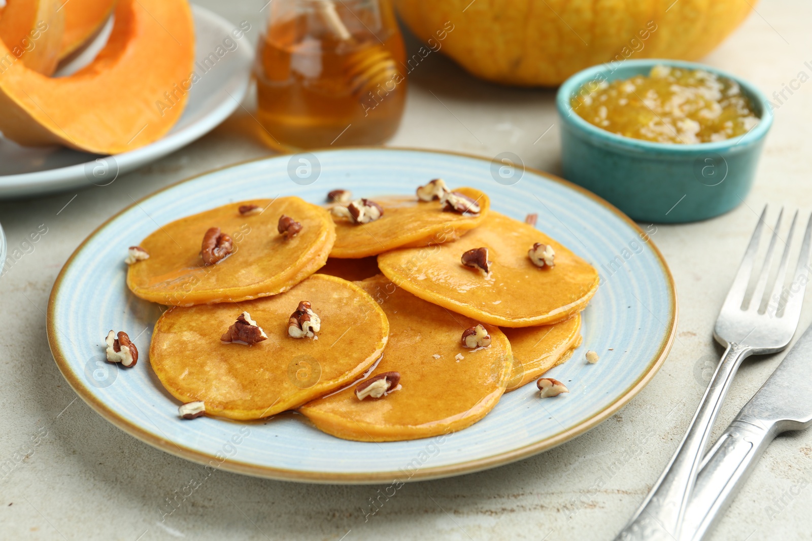 Photo of Tasty pumpkin pancakes with nuts, jam and honey on light grey table, closeup