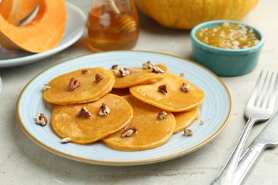 Photo of Tasty pumpkin pancakes with nuts, jam and honey on light grey table, closeup