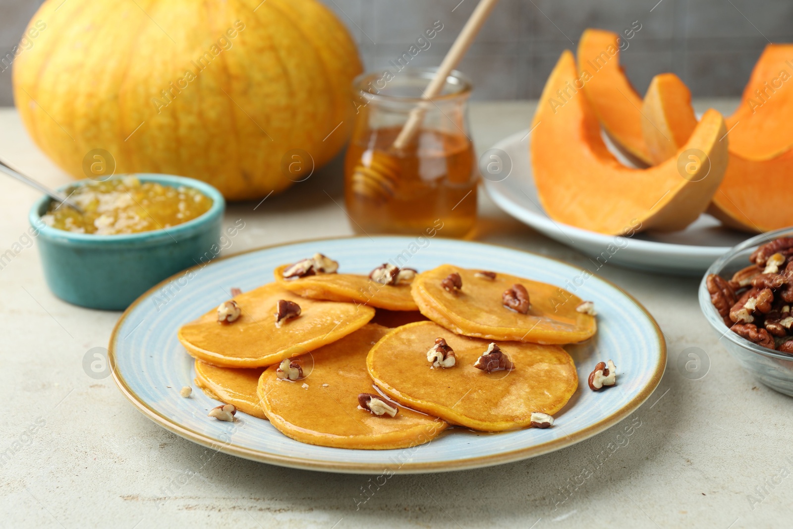 Photo of Tasty pumpkin pancakes with nuts, jam and honey on light grey table, closeup