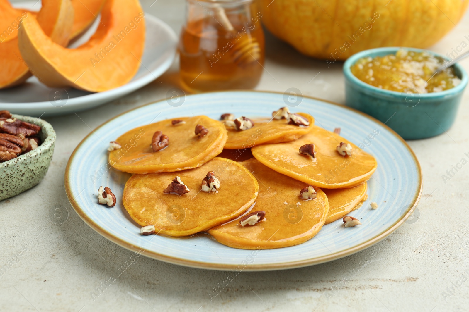 Photo of Tasty pumpkin pancakes with nuts, jam and honey on light grey table, closeup