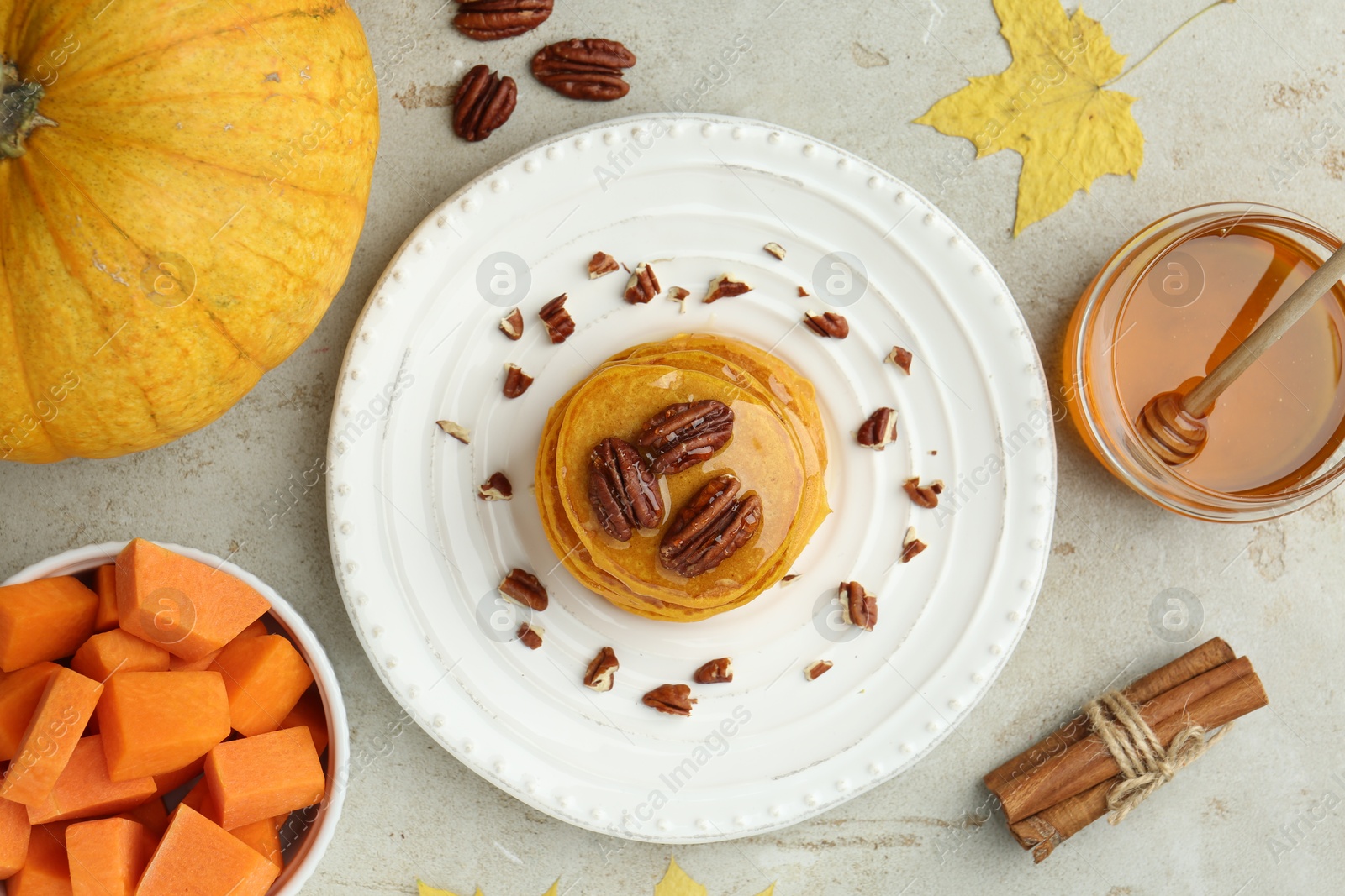 Photo of Tasty pumpkin pancakes with nuts and honey served on light grey table, flat lay