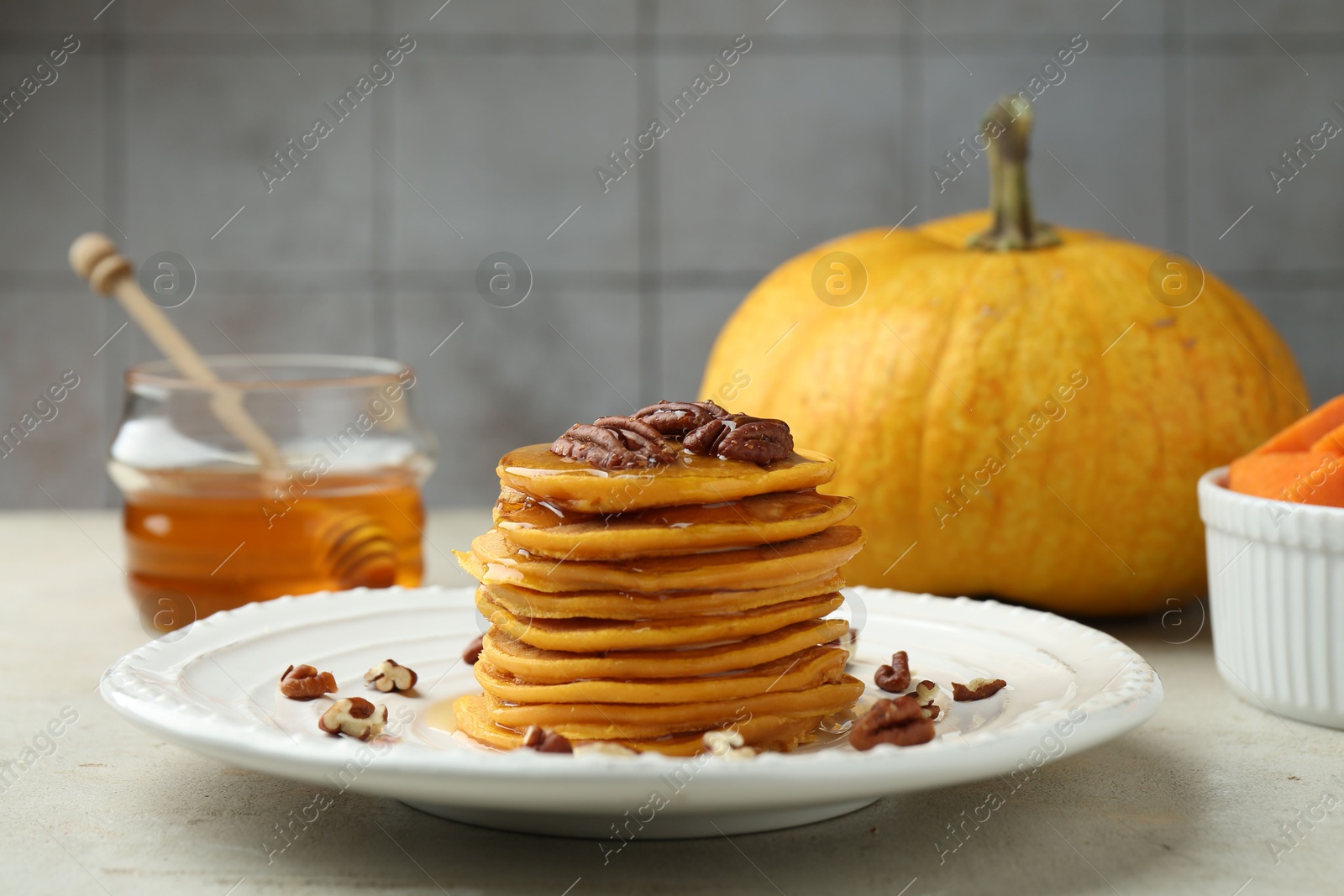 Photo of Tasty pumpkin pancakes with nuts and honey on light grey table, closeup