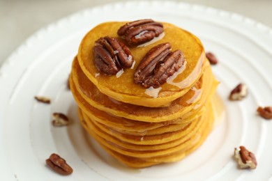 Photo of Tasty pumpkin pancakes with nuts and honey on plate, closeup