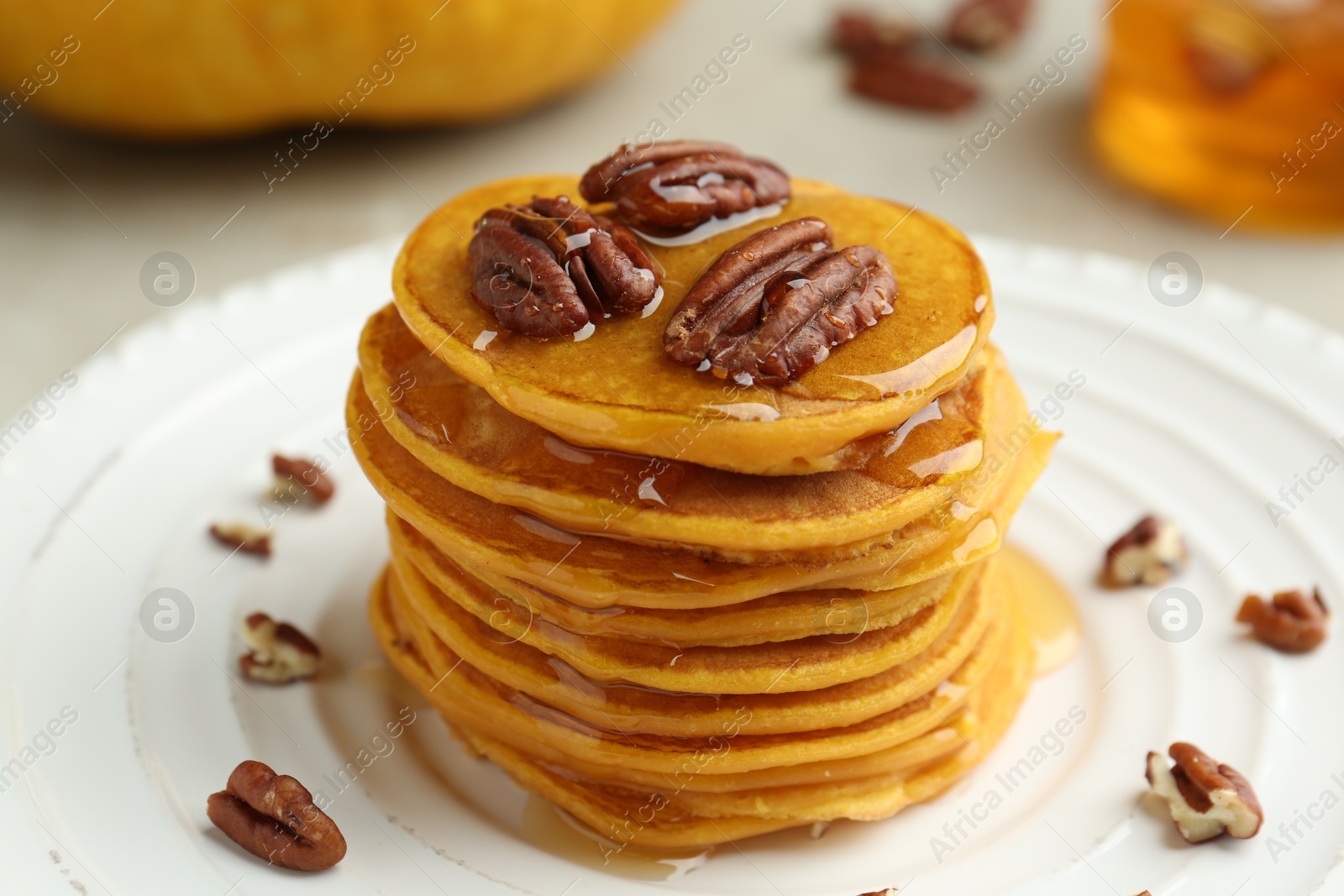 Photo of Tasty pumpkin pancakes with nuts and honey on plate, closeup