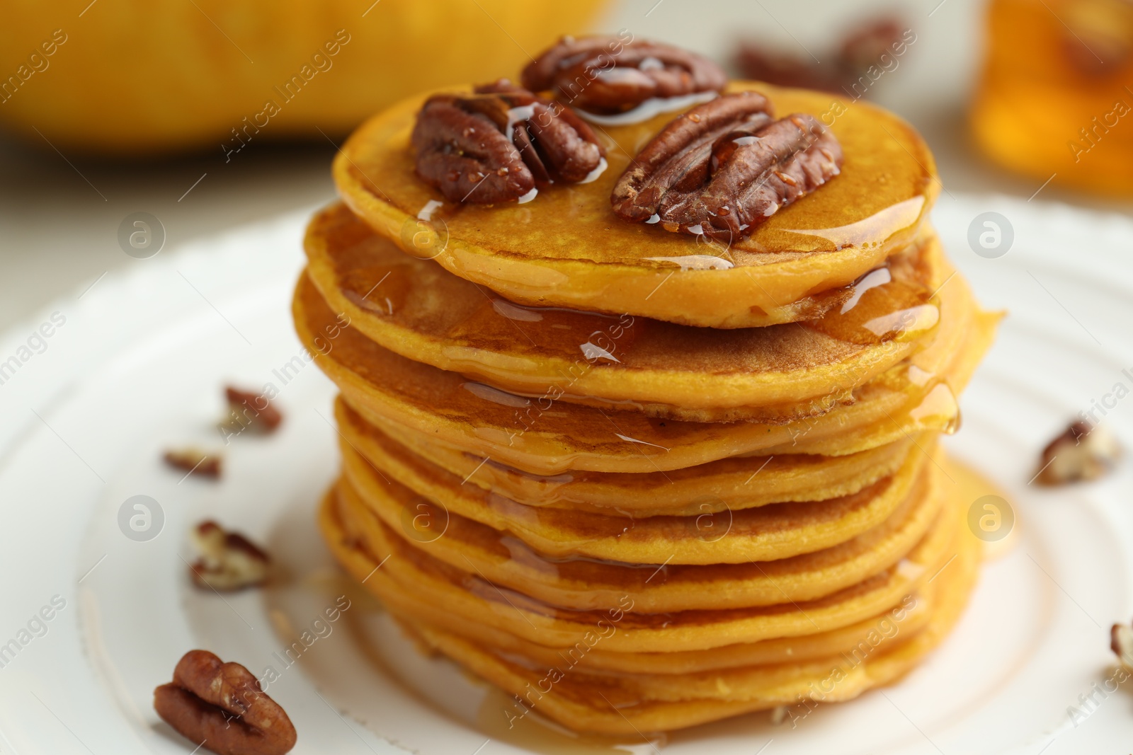 Photo of Tasty pumpkin pancakes with nuts and honey on plate, closeup