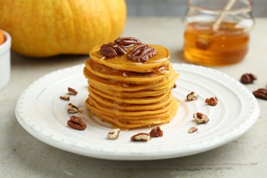 Tasty pumpkin pancakes with nuts and honey on light grey table, closeup