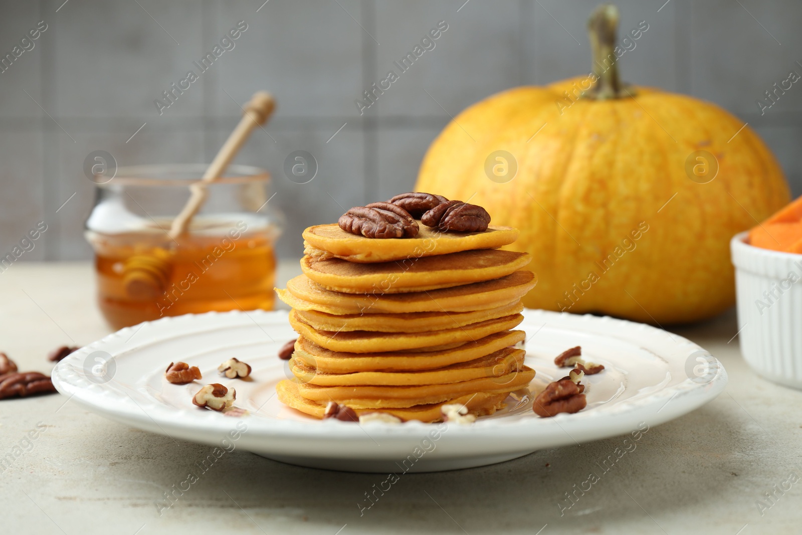 Photo of Tasty pumpkin pancakes with nuts and honey on light grey table, closeup